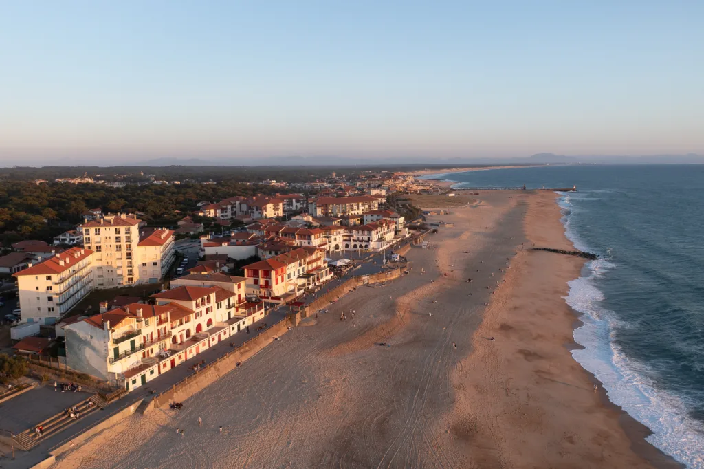 Coucher de soleil sur la Plage centrale d’Hossegor, vue depuis la place des Landais, avec l’océan Atlantique illuminé par des teintes dorées et orangées.
